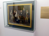A photo of the Charles Bowman and Family painting in an enclosed glass case.